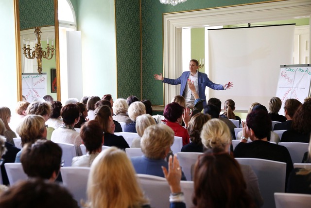 Ein Firmenevent im Schönbornsalon. Der Redner ist seinen Zuhörern zugewandt, im Hintergrund sehen wir seine Materialien und Präsentationsutensilien wie Leinwand und Whiteboard.