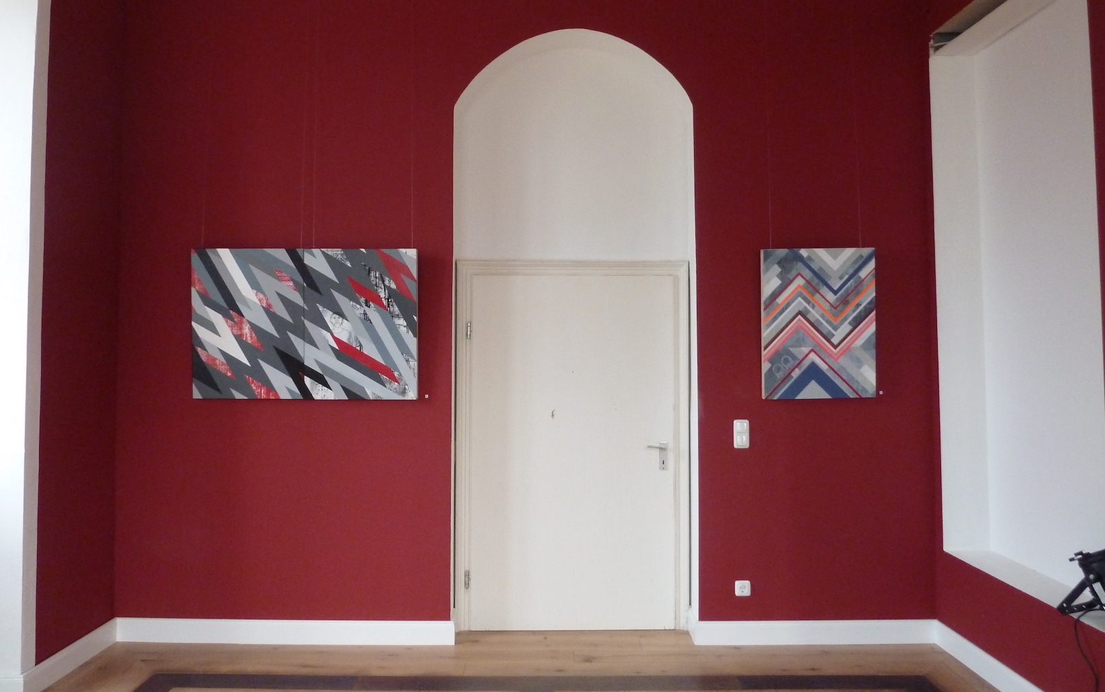 Kunstausstellung mit geografischen Gemälden im roten Salon. Die Gemälde befinden sich an der Wand, zwischen Ihnen ist eine weisse Eingangstür.