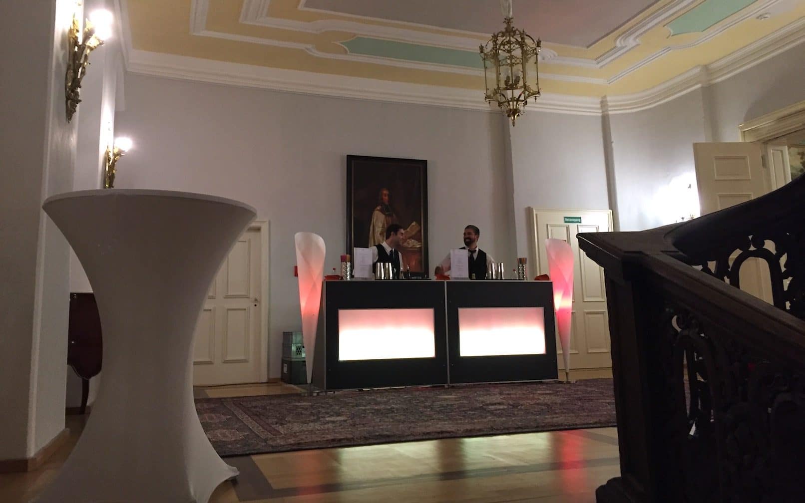 Schlossempfang im Foyer. Zwei Servicekräfte kümmern sich um das Wohl der Gäste und stehen hinter der Bar bereit.