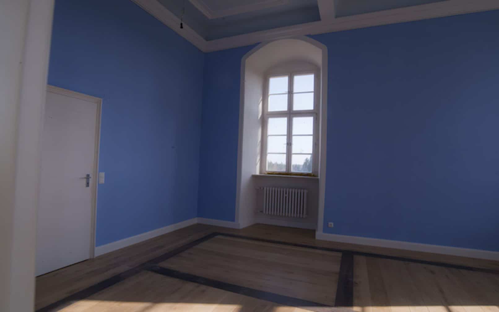 Das leerstehende blaue Schlosszimmer mit einem Fenster und einer Tür links.