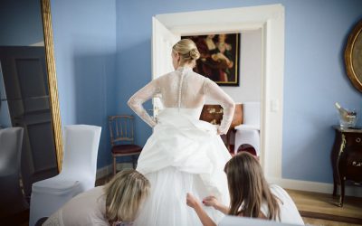 frau im brautkleid und zwei frauen helfen beim anziehen